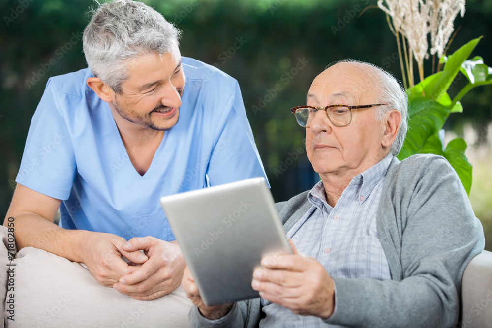 Male Caretaker Looking At Senior Man Using Tablet Computer Male Caretaker Looking At Senior Man Using Tablet Computer
