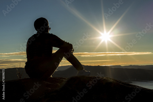 Billede på lærred Silhouette man on a mountain enjoying the view at sunset