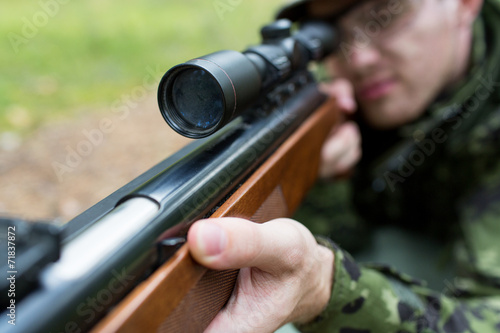close up of soldier or hunter with gun in forest