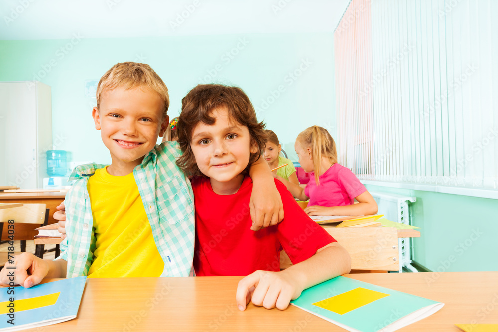 Two boys hugging and sitting together in classroom