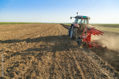 фотографія Farmer plowing stubble field with red tractor
