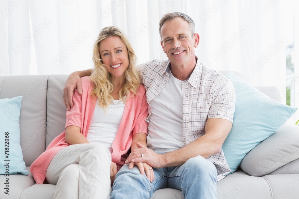 Happy couple relaxing on the couch smiling at camera Happy couple relaxing on the couch smiling at camera