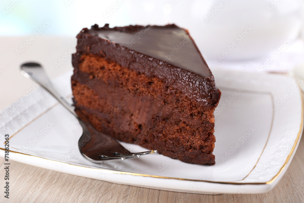 Piece of chocolate cake on saucer on teapot background Piece of chocolate cake on saucer on teapot background