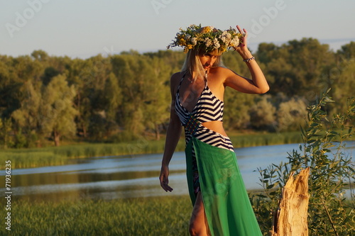 Девушка с венком на голове стоит на бревне около болото