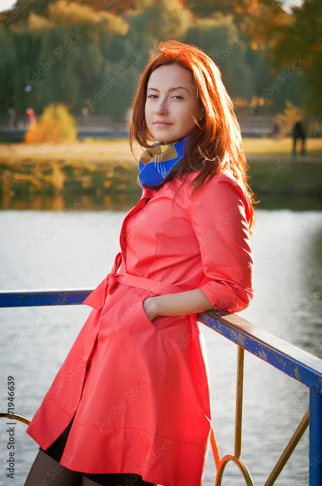 Woman in a coral coat walks on autumn park