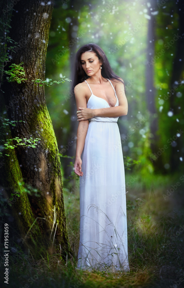 Lovely young lady wearing an elegant long white dress in forest
