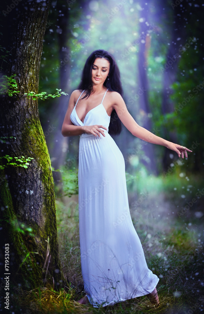 Lovely young lady wearing an elegant long white dress in forest Lovely young lady wearing an elegant long white dress in forest
