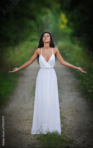 Lovely young lady wearing an elegant long white dress in forest