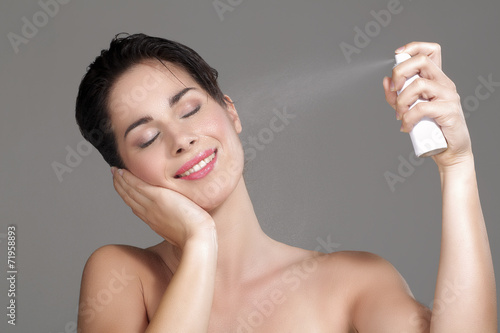 Beautiful woman applying spray water on face