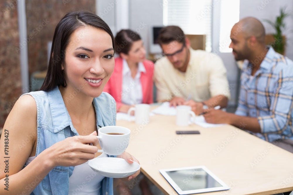 Woman drinking a coffee while his colleague work behind her Woman drinking a coffee while his colleague work behind her