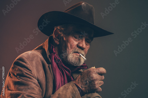Old rough western cowboy with gray beard and brown hat lighting