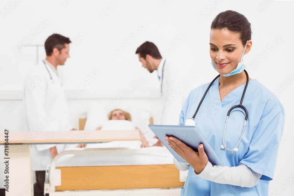 Doctor using digital tablet with colleagues and patient behind Doctor using digital tablet with colleagues and patient behind