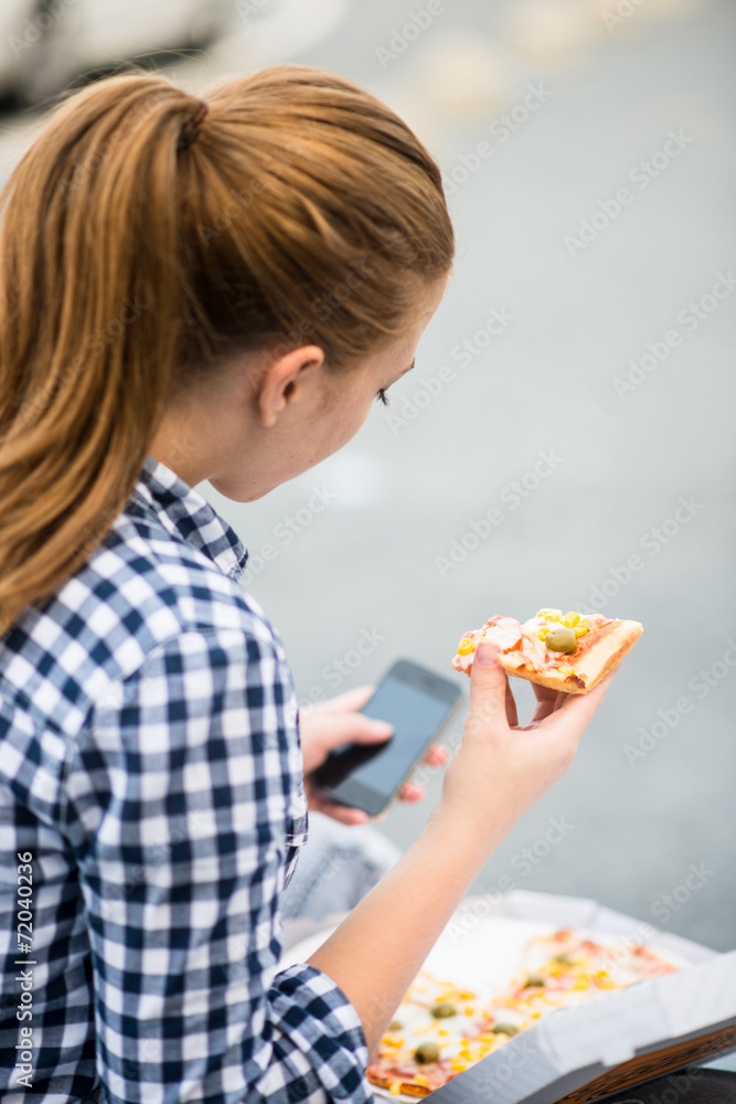 Teenager eating pizza looking in phone Teenager eating pizza looking in phone