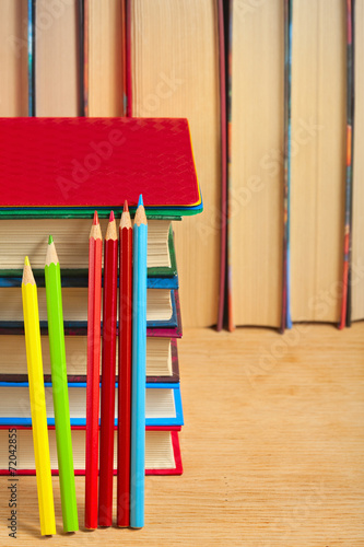 Pile of books and colored pencils on a wooden surface against th