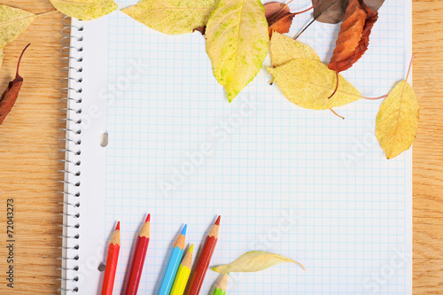 Notebook with colored pencils and autumn leaves on a wooden surf