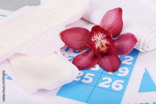 Fototapeta Naklejka Na Ścianę i Meble -  Sanitary pads and lilac orchid on blue calendar background
