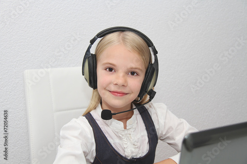 Llittle girl sits in front of a laptop with headphones and learn