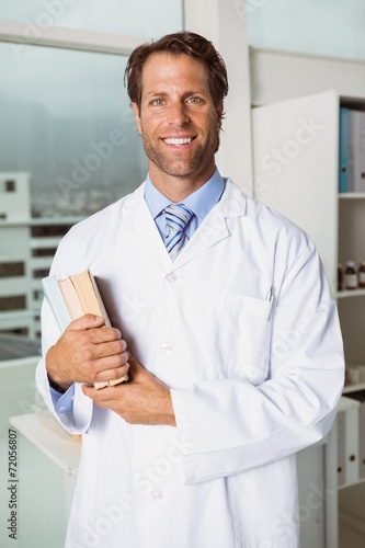 Smiling male doctor holding books in medical office