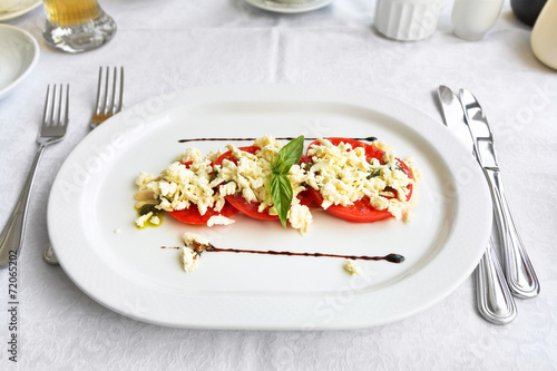 tomato with sheep cheese and basil on white plate