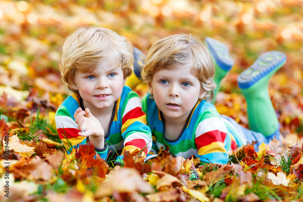 Two little kid boys laying in autumn leaves in colorful clothing Two little kid boys laying in autumn leaves in colorful clothing