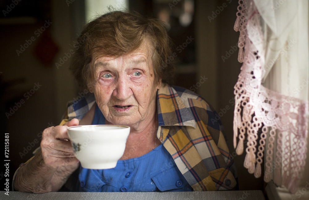 Old woman drinking tea at the window in his house.. Old woman drinking tea at the window in his house..
