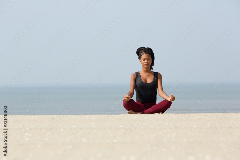 African woman sitting at beach in yoga pose