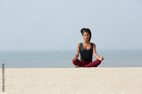 African american woman sitting at beach in yoga pose