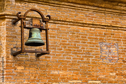 Ancient church bell fixed on rusty metal frame on brick wall