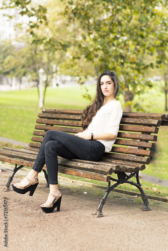 Elegant beautiful woman sitting on bench in the park.