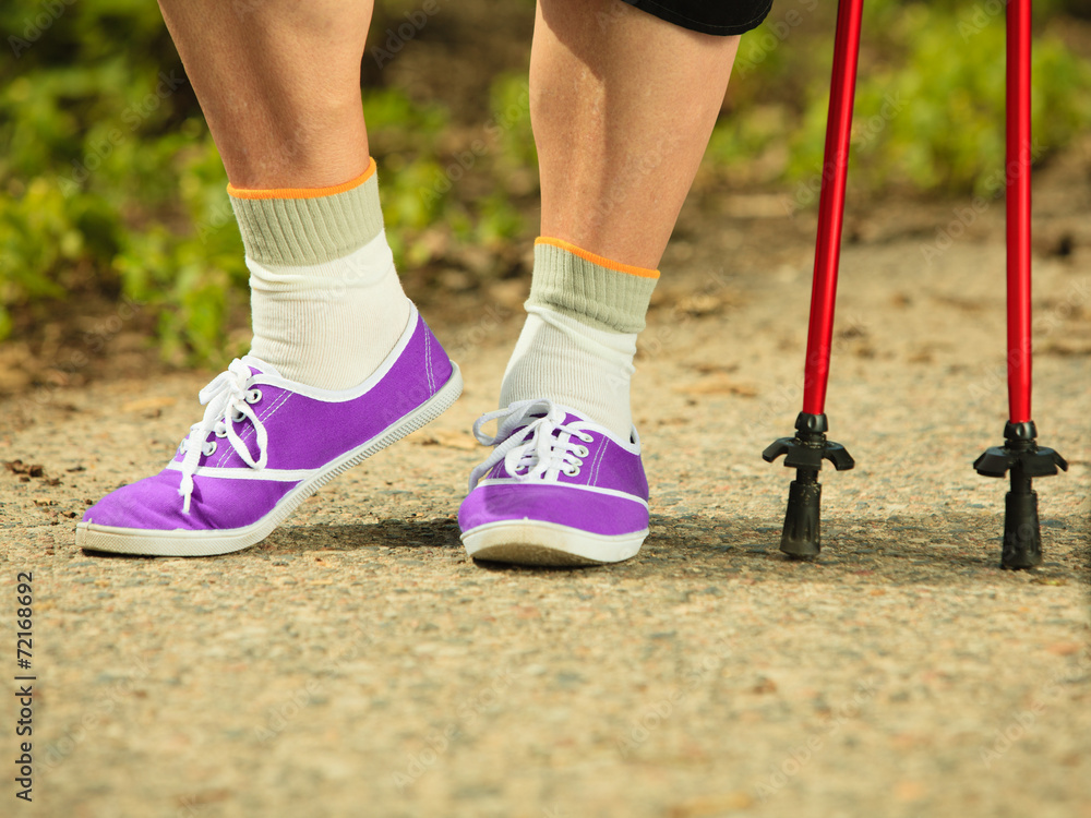 active senior legs in sneakers nordic walking in a park.