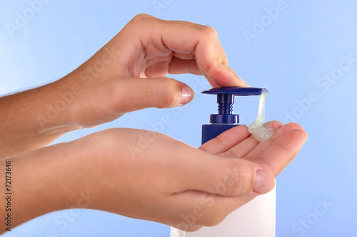 Female hands using liquid soap on light blue background