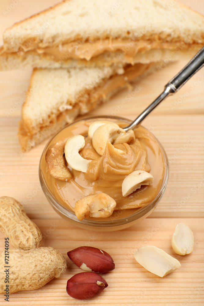 Fototapeta premium Creamy peanut butter in bowl and bread slices on wooden table