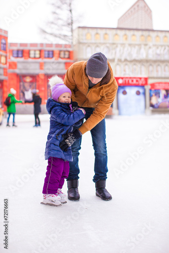 Young dad and adorable little girl have fun on skating rink