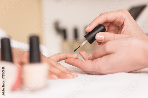 Woman in nail salon receiving manicure by beautician.