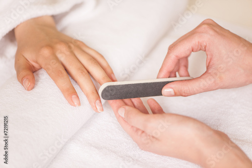 Woman in nail salon receiving manicure by beautician.