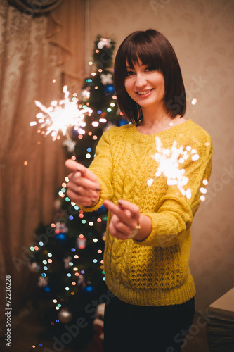 Young woman holding sparkles in her hands near christmas tree © polinaloves