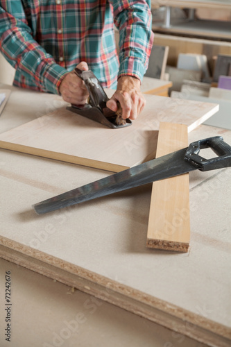 Midsection Of Carpenter Using Planer At Workbench