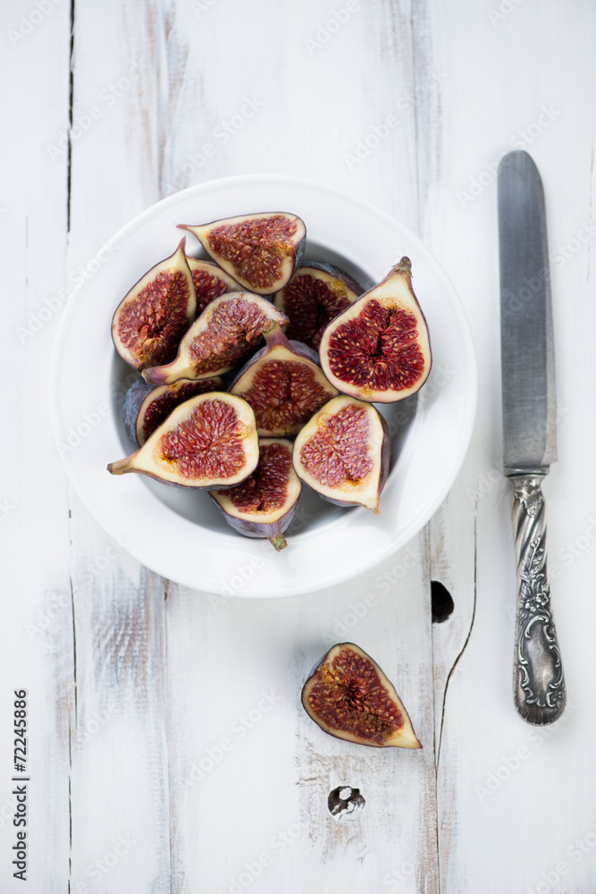 Sliced ripe figs in a plate over white wooden background