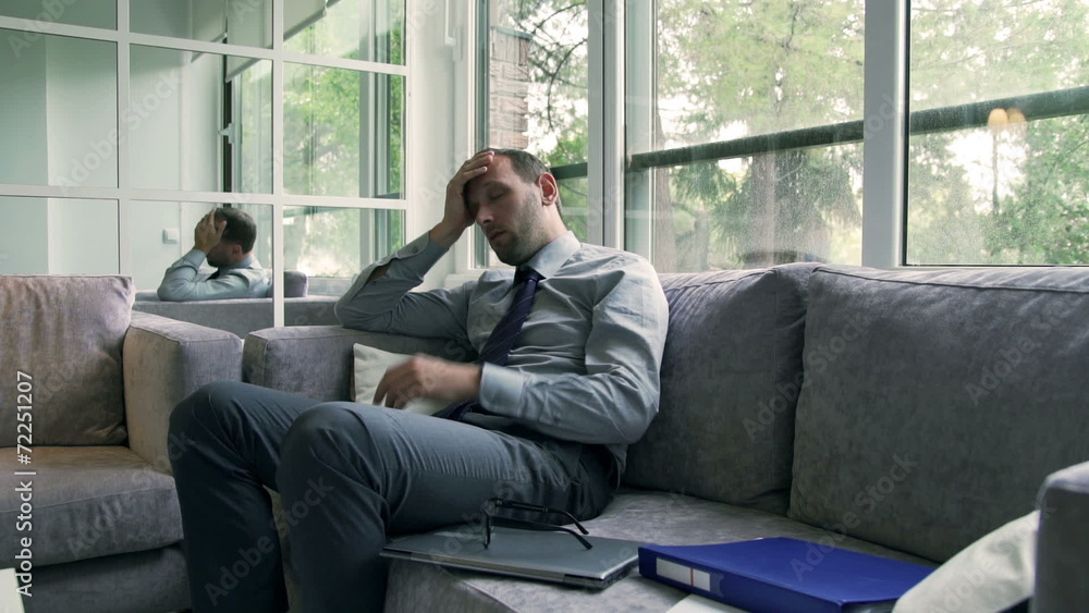 Sad businessman sitting on the sofa and massaging head Sad businessman sitting on the sofa and massaging head