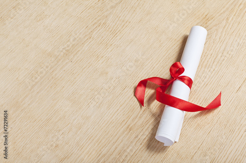 Scroll of paper with a red ribbon on a wooden surface.