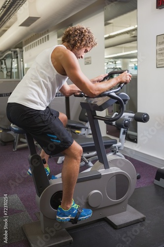 Side view of man working out on exercise bike at gym