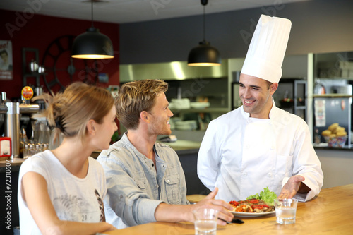 Young chef serving cooked dish to customers