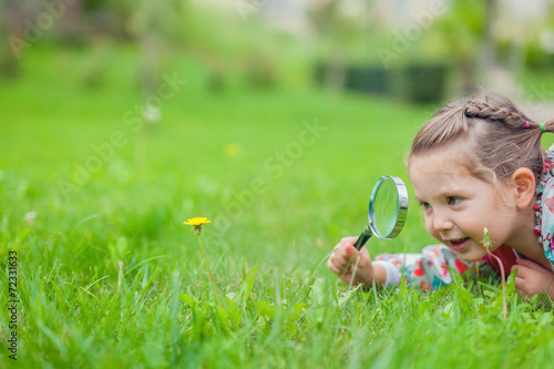 little cute girl with magnifying glass examining flower