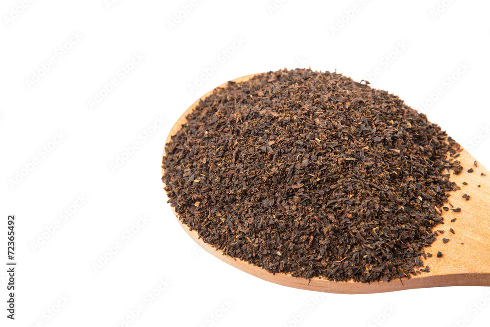 Dried, processed tea leaves in wooden spoon over white Dried, processed tea leaves in wooden spoon over white
