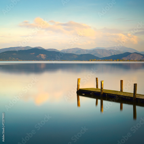 Fototapeta Naklejka Na Ścianę i Meble -  Wooden pier or jetty and on a blue lake sunset and sky reflectio