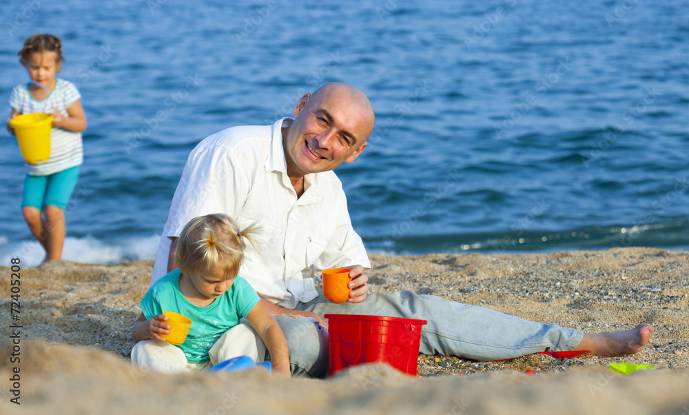 Fototapeta premium Girls playing with sand next to dad