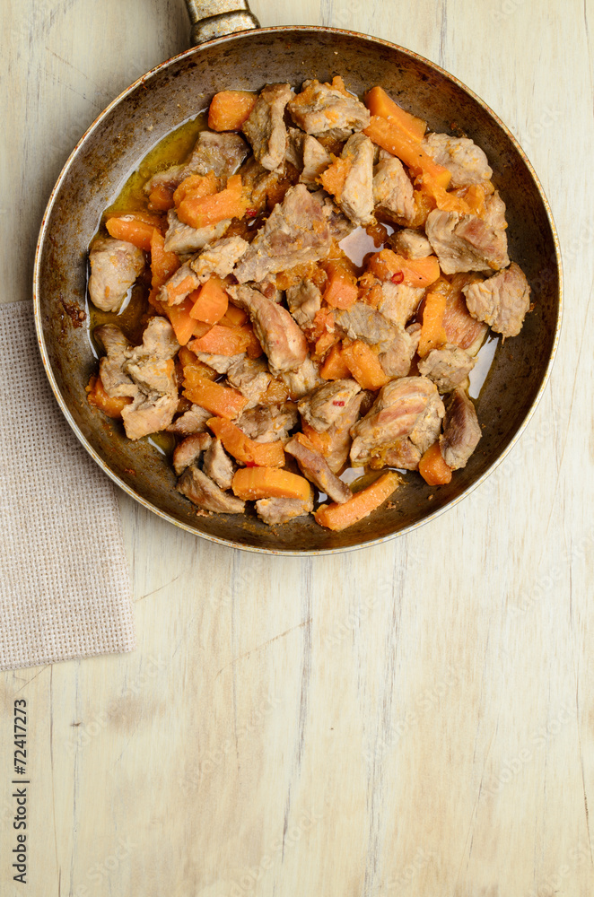 Fried pieces of meat and pumpkin in a pan on a wooden table Fried pieces of meat and pumpkin in a pan on a wooden table