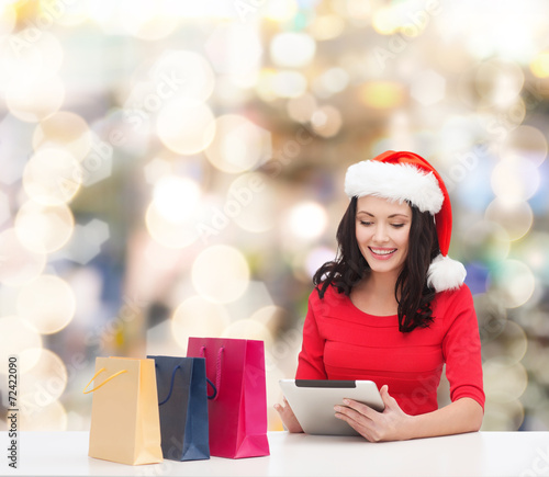 smiling woman in santa hat with bags and tablet pc