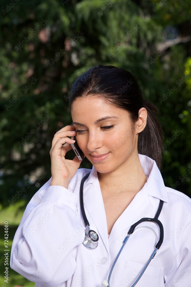 doctor young woman talking mobile over a green trees background. doctor young woman talking mobile over a green trees background.