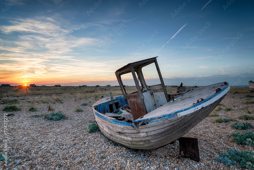 Wooden fishing boat with nets washed up on a shingle beach
